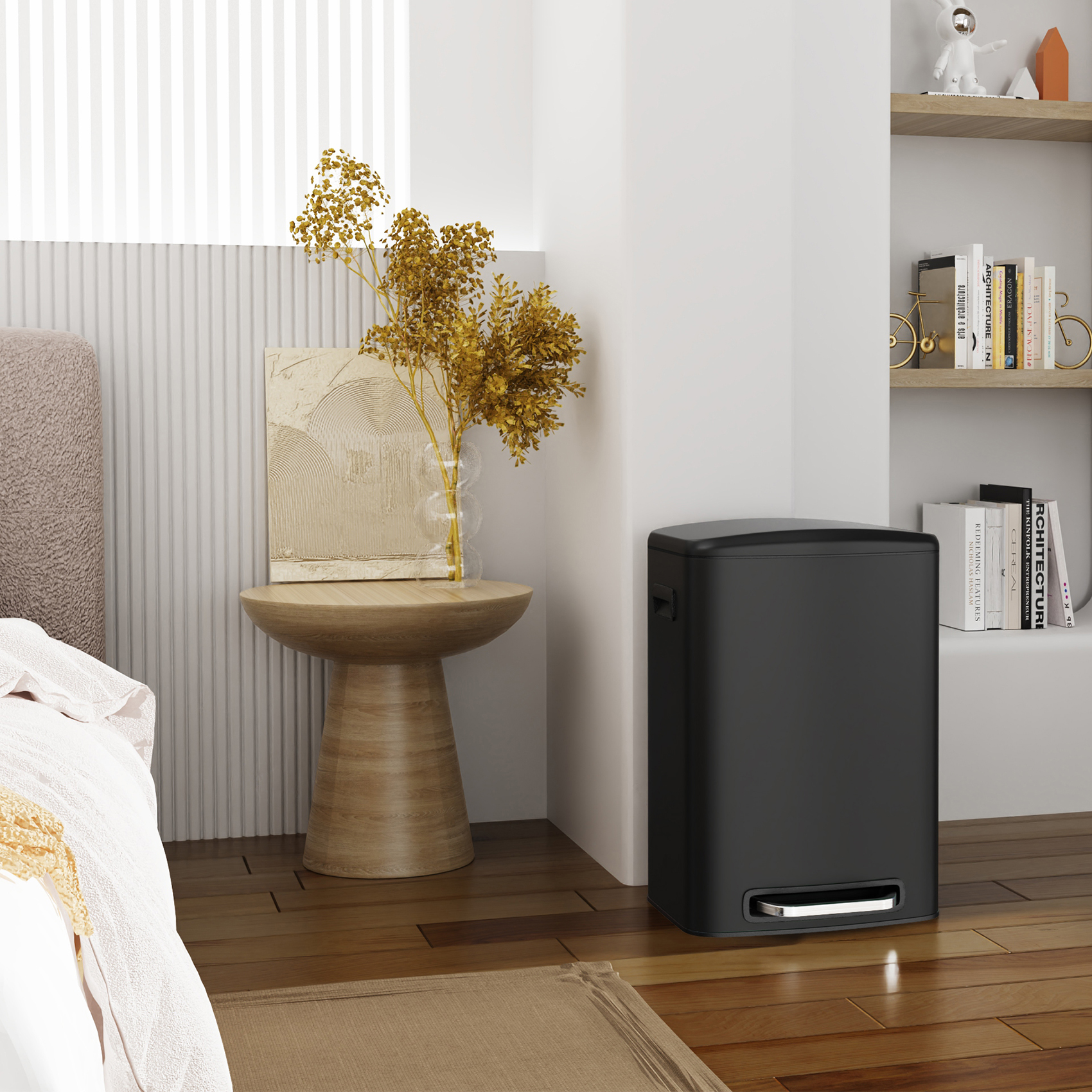 A modern living room showcases a stainless steel foot pedal-operated, soft-close trash can with a 13-gallon capacity next to a small wooden side table. On the table, yellow dried flowers in a vase complement a framed abstract art piece, while shelves filled with books and decor enhance the background.